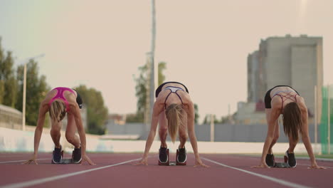 Primer-Plano,-Tres-Atletas-Femeninas-De-Pista-Y-Agua-En-La-Línea-De-Salida-De-La-Competición-Del-Estadio-Se-Preparan-Y-Huyen-En-Una-Carrera-De-Sprint.